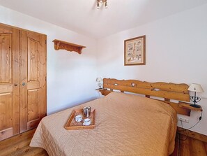 A bedroom with a wooden bed, a wooden wardrobe, a bedside table with a lamp, and a tray with cups and a pot on the bed. - Spacious apartment with terrace - 4 guests (Les Menuires)