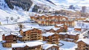 A snow-covered resort with multiple wooden buildings, ski lifts, and a mountainous backdrop. - Spacious apartment with terrace - 4 guests (Les Menuires)