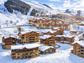 A snow-covered resort with multiple wooden buildings, ski lifts, and a mountainous backdrop. - Spacious apartment with terrace - 4 guests (Les Menuires)