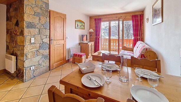 A dining area with a stone wall, wooden furniture, and a view through large windows. - Spacious apartment with terrace - 4 guests (Les Menuires)