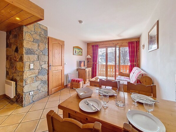 A dining area with a stone wall, wooden furniture, and a view through large windows. - Spacious apartment with terrace - 4 guests (Les Menuires)
