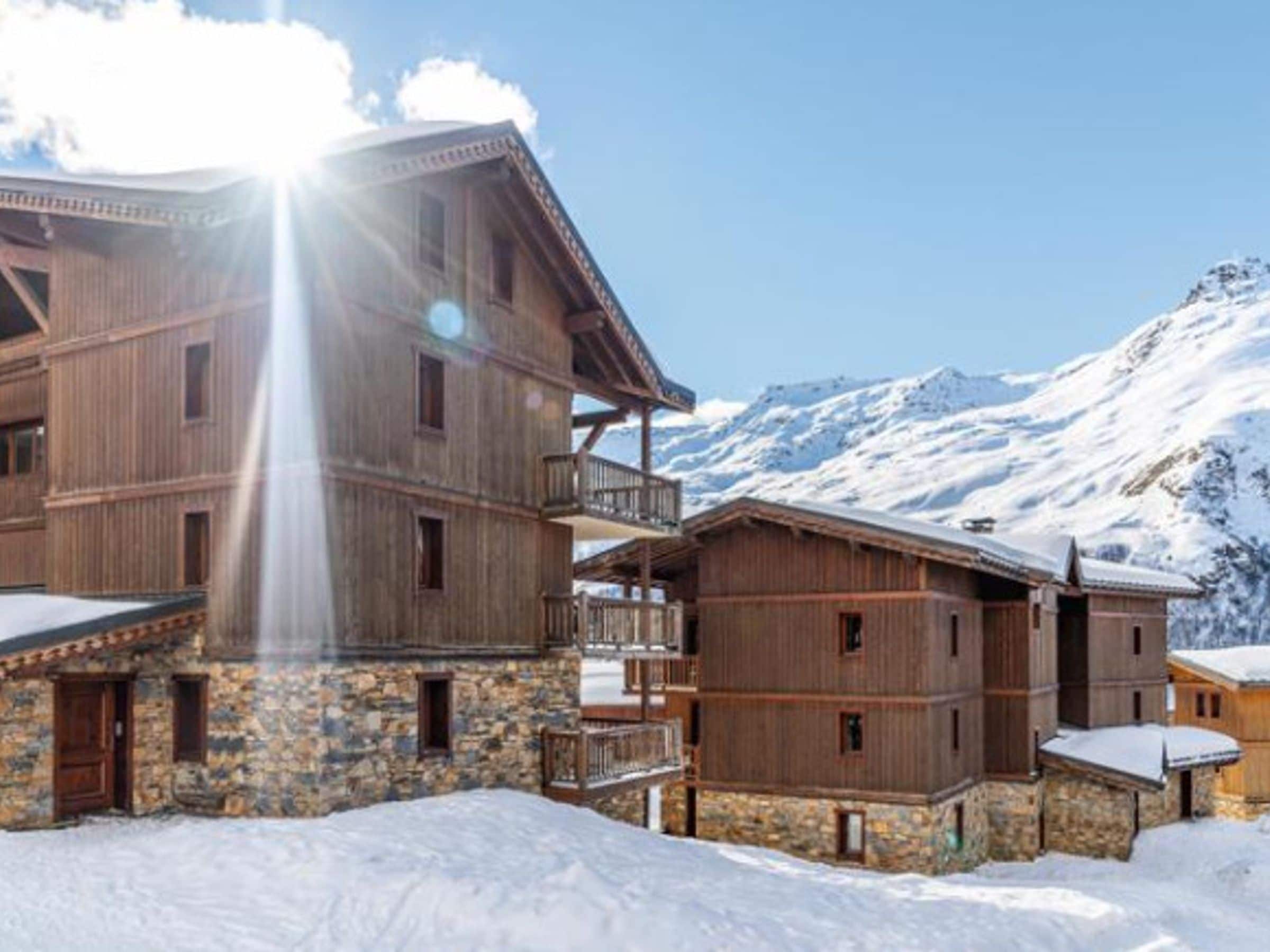 Ein mehrstöckiges Holzgebäude mit Balkonen vor einer verschneiten Berglandschaft.