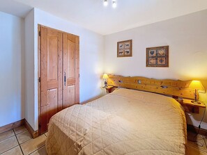 A bedroom with a large bed, wooden headboard, two wall-mounted lamps, and a door. - Spacious apartment near slopes - 6 guests (Les Menuires)