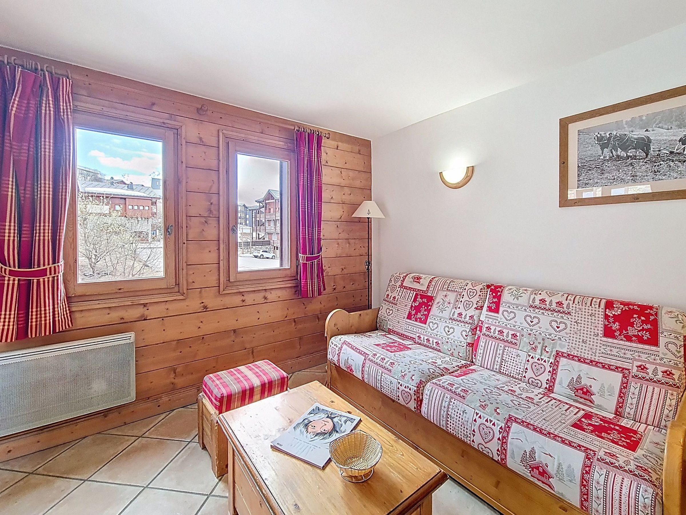 Um quarto acolhedor com decoração em madeira, um sofá estampado, uma mesinha com um livro e uma janela com cortinas.