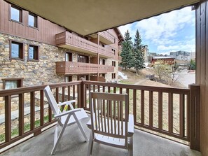 A balcony with two white chairs, a stone building with balconies, and a view of a snowy mountain. - Spacious apartment near slopes - 6 guests (Les Menuires)
