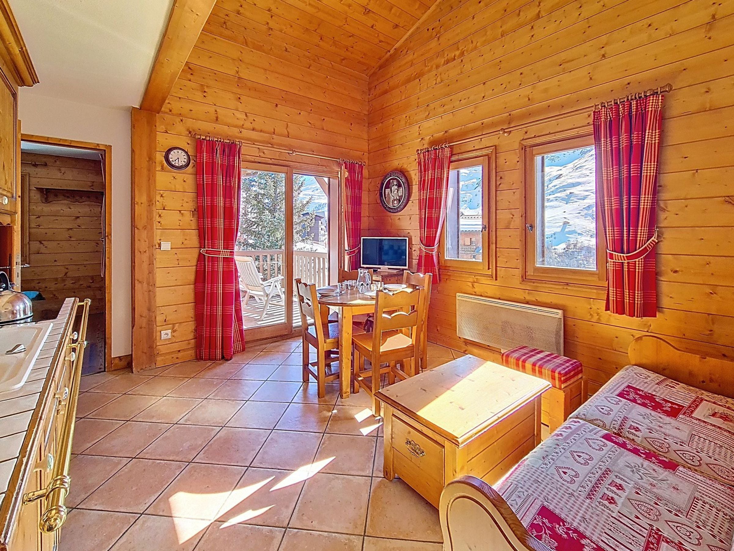 Ein Interieur einer Holzhütte mit Essbereich, einer Couch, einem Fernseher und einem Fenster mit Vorhängen.