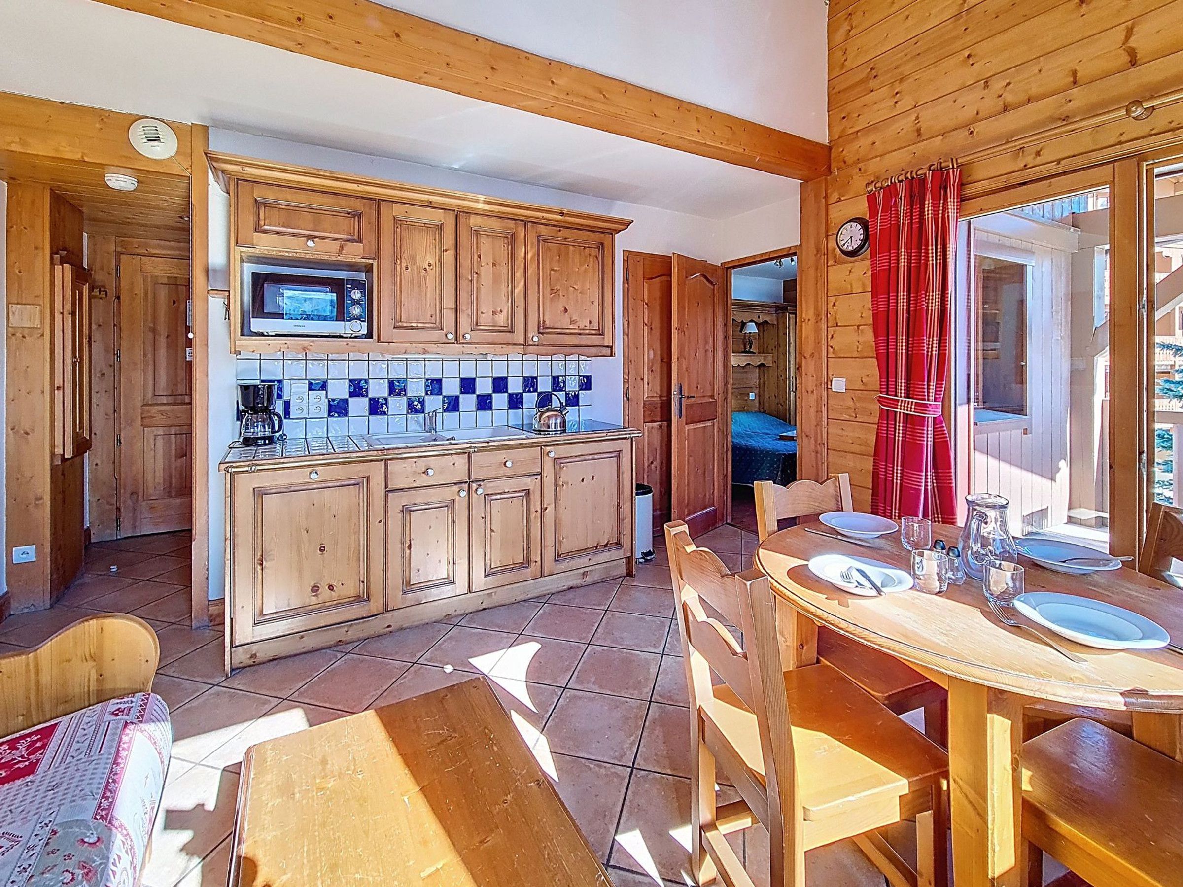 A wooden interior with a kitchen area, a dining table set for two, and a view through a window.