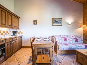A cozy kitchen with wooden cabinets, a tiled backsplash, a dining table set with plates and glasses, and a patterned sofa. - Spacious apartment near slopes - 6 guests (Les Menuires)