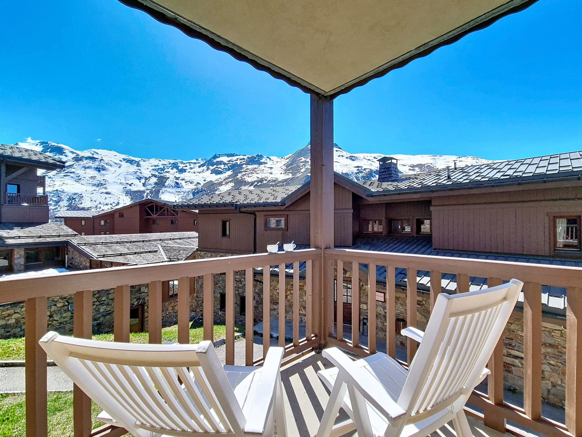A balcony with two white chairs, a stone wall, and a view of snow-capped mountains.