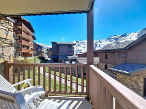 Ein Balkon mit Blick auf schneebedeckte Berge, Steinhäuser und einen strahlend blauen Himmel.