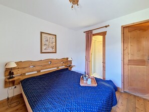 Ein Schlafzimmer mit einem hölzernen Kopfende, einem Bett mit einer blaublau gepunkteten Tagesdecke, einem Nachttisch mit einer Lampe und einem gerahmten Bild an der Wand.