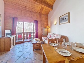 Ein Holzinterieur mit einem für zwei Personen gedeckten Esstisch, einer Couch und einem Fernseher auf einem Schrank.