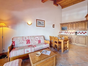 Ein gemütliches Wohnzimmer mit einer Couch, einem Holzespeisetisch und Stühlen, eine Küche mit Holdekor-Schränken und einer gefliesten Spritzwand sowie eine Lampe.