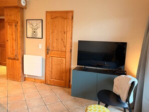 A room with a wooden door, a framed picture on the wall, a television on a cabinet, and a chair with a towel. - Spacious apartment, terrace, pets welcome - 4 guests (Les Menuires)