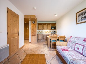 A cozy living room with a wooden sofa, a dining table with chairs, and a kitchen area with wooden cabinets and a microwave. - Bright apartment near slopes - 4 guests (Les Menuires)