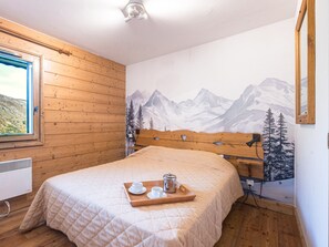 A bedroom with a wooden headboard, a mountain mural on the wall, a window with a view, and a tray with cups and a pot on the bed. - Bright apartment near slopes - 4 guests (Les Menuires)