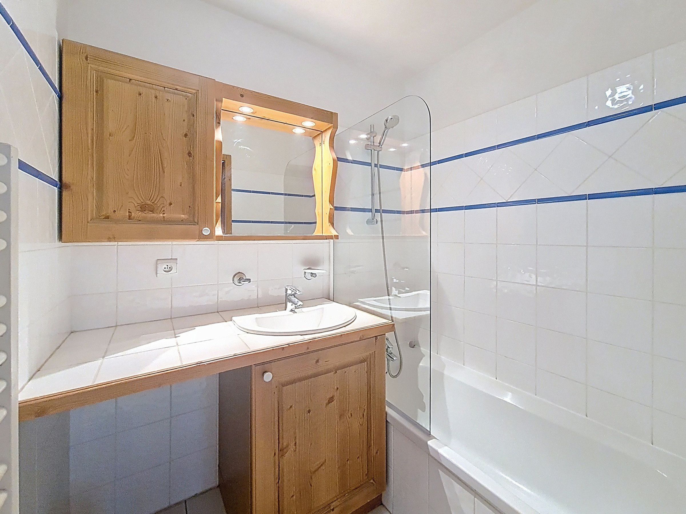 A bathroom with a wooden vanity, a mirror, a sink, and a shower.