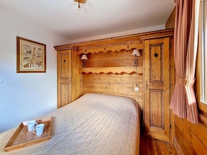 Ein hölzernes Bett mit einer gesteppten Matratze, zwei Nachttischlampen und einem Tablett mit zwei Tassen.
