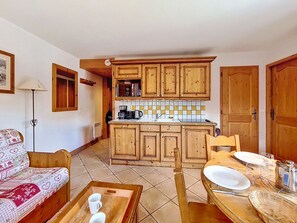 A compact kitchen with wooden cabinets, a tiled backsplash, and a dining area with a table set for two. - Bright apartment near slopes - 4 guests (Les Menuires)