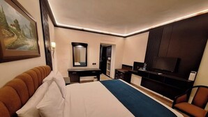 A hotel room with a bed, a desk, a chair, a television, and a painting on the wall.