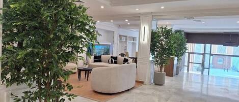 A spacious lobby with a large potted plant, a curved white sofa, and a view through a glass door.
