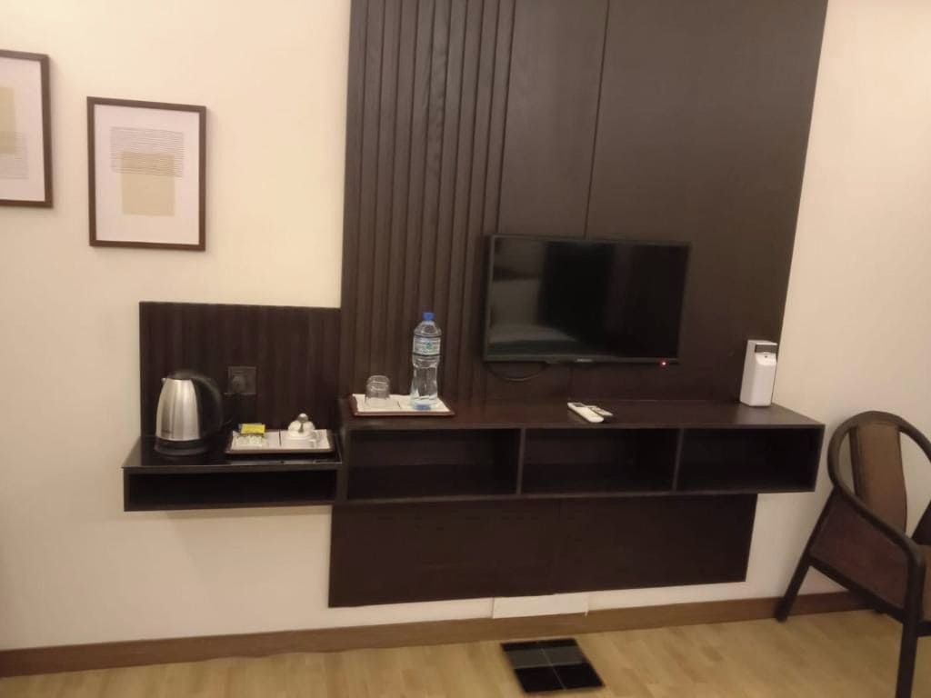 Habitación de hotel con mueble de madera oscura, televisión de pantalla plana, una botella de agua, hervidor de agua y un control remoto.
