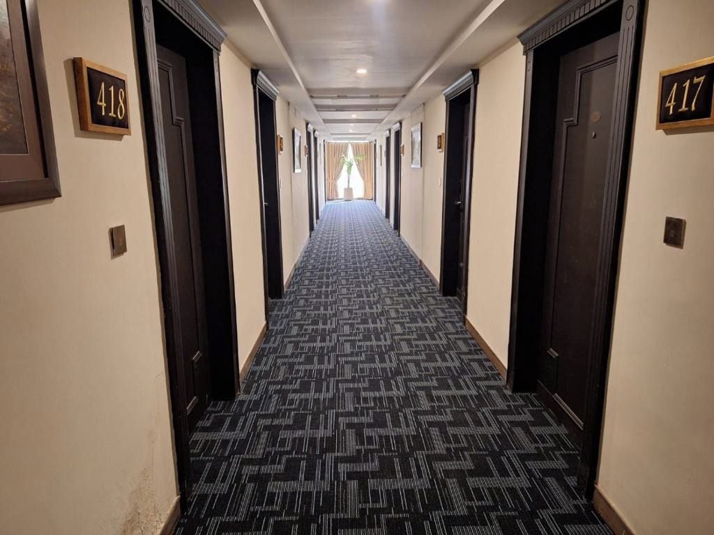 A hotel hallway with carpeted floors, doors numbered 418 and 417, and a view into a room at the end.