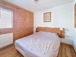 Ein Schlafzimmer mit einer Wand aus Holzlatten, einem Bett mit gemustertem Überwurf, einem Nachttisch mit Lampe und einem gerahmten Bild an der Wand.