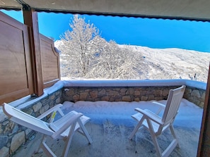 Ein mit Schnee bedeckter Außenbereich mit Sitzgelegenheit, Steinmauern und Blick auf eine verschneite Landschaft.