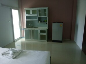 A small, clean room with a kitchenette, a bed with a white comforter, and a door leading to another room. - bed room with full facture nd air-condition (Bang Lamung District, Chon Buri Province)