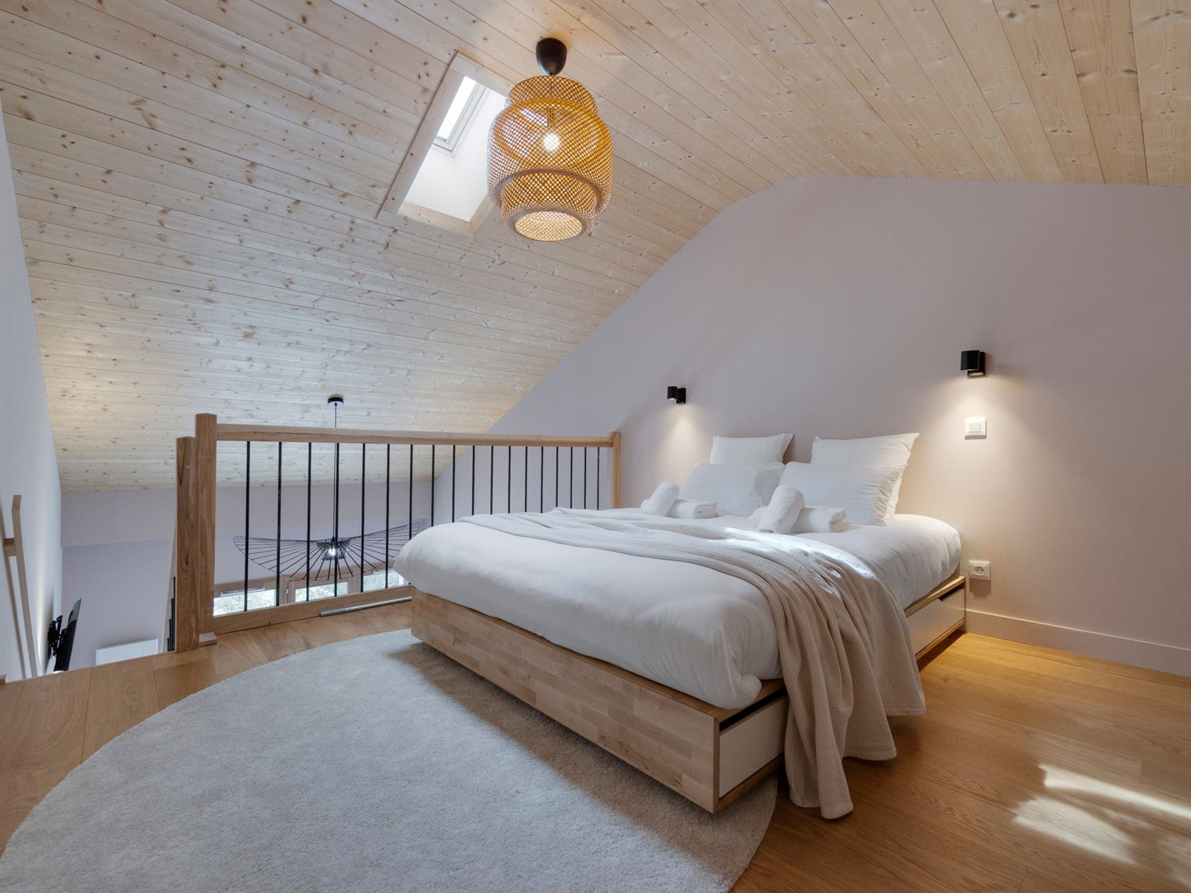 A bedroom with a sloped ceiling, a bed with white bedding, a wooden floor, and a skylight.
