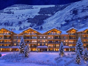 Ein mehrstöckiges Chalet mit Balkonen, umgeben von schneebedeckten Bäumen und einer Bergkulisse.