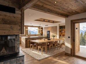 Eine moderne Küche mit Holzbalken, einem Essbereich mit großem Tisch und Stühlen sowie Bergblick durch die Fenster.