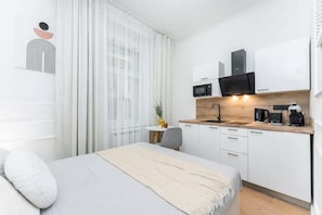 Une chambre d’hôtel moderne et minimaliste, équipée d’un lit, d’une petite table à manger et d’une kitchenette.