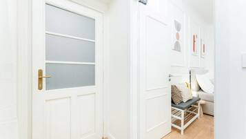 A hallway with a white door featuring a frosted glass panel, a white wall with a door, and a bed with a white frame and a pillow.