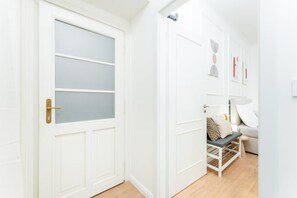 A hallway with a white door featuring a frosted glass panel, a white wall with a door, and a bed with a white frame and a pillow.