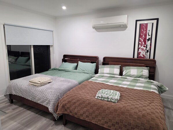 A bedroom with two beds, a window with blinds, an air conditioning unit, and a decorative wall piece.
