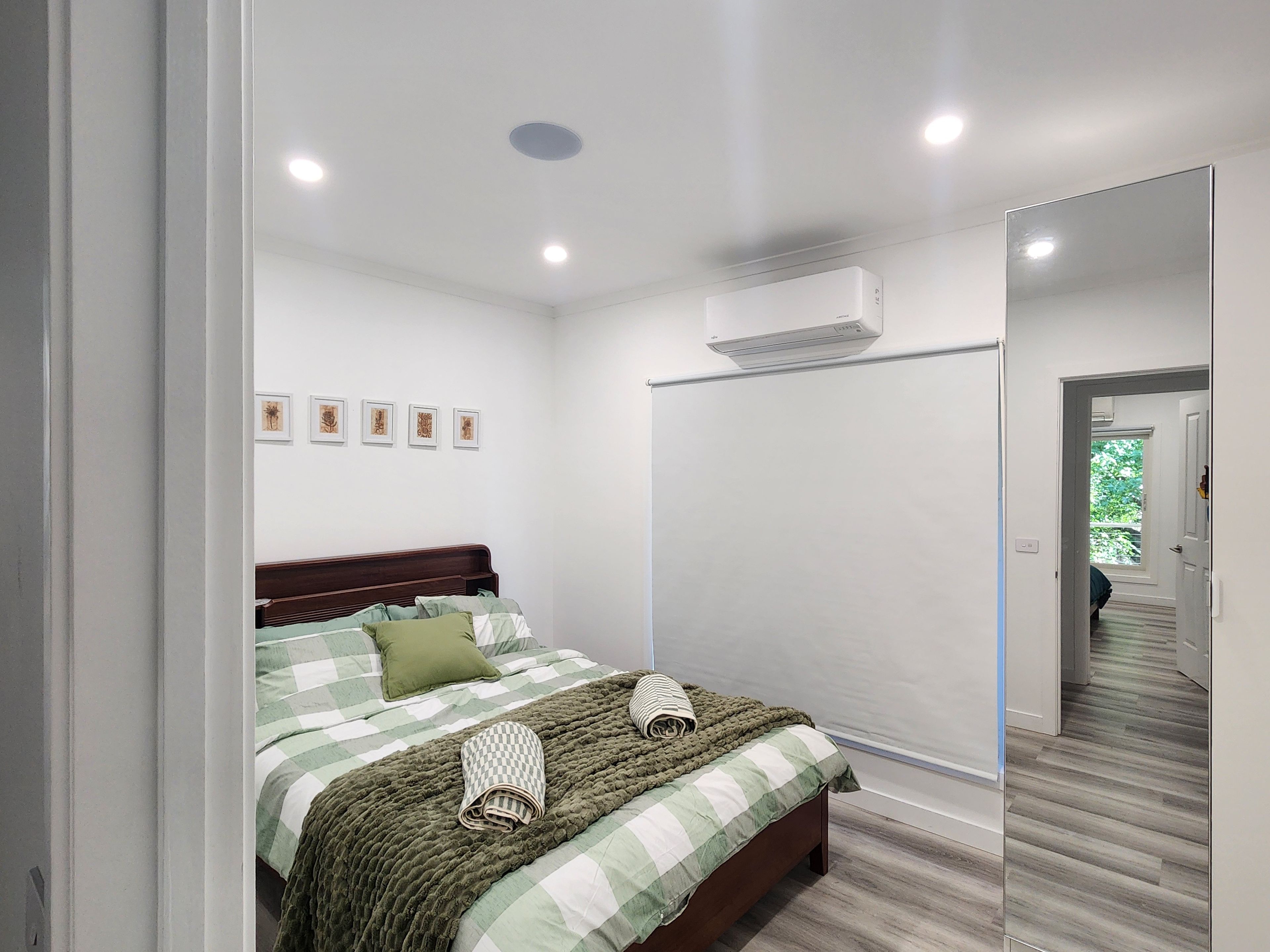 A bedroom with a bed, a mirror, an air conditioning unit, and a hallway leading to another room.