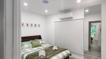 A bedroom with a bed, a mirror, an air conditioning unit, and a hallway leading to another room.