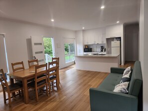 A modern kitchen with white cabinets, a dining area with wooden chairs, and a green sofa.