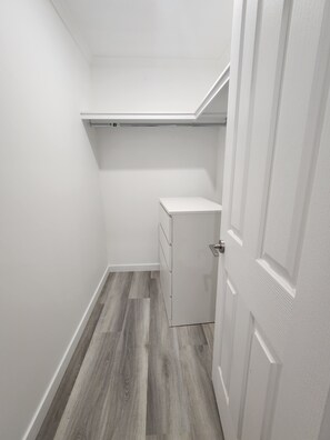 A narrow hallway with a wooden floor, a white door, and a white storage unit with drawers.