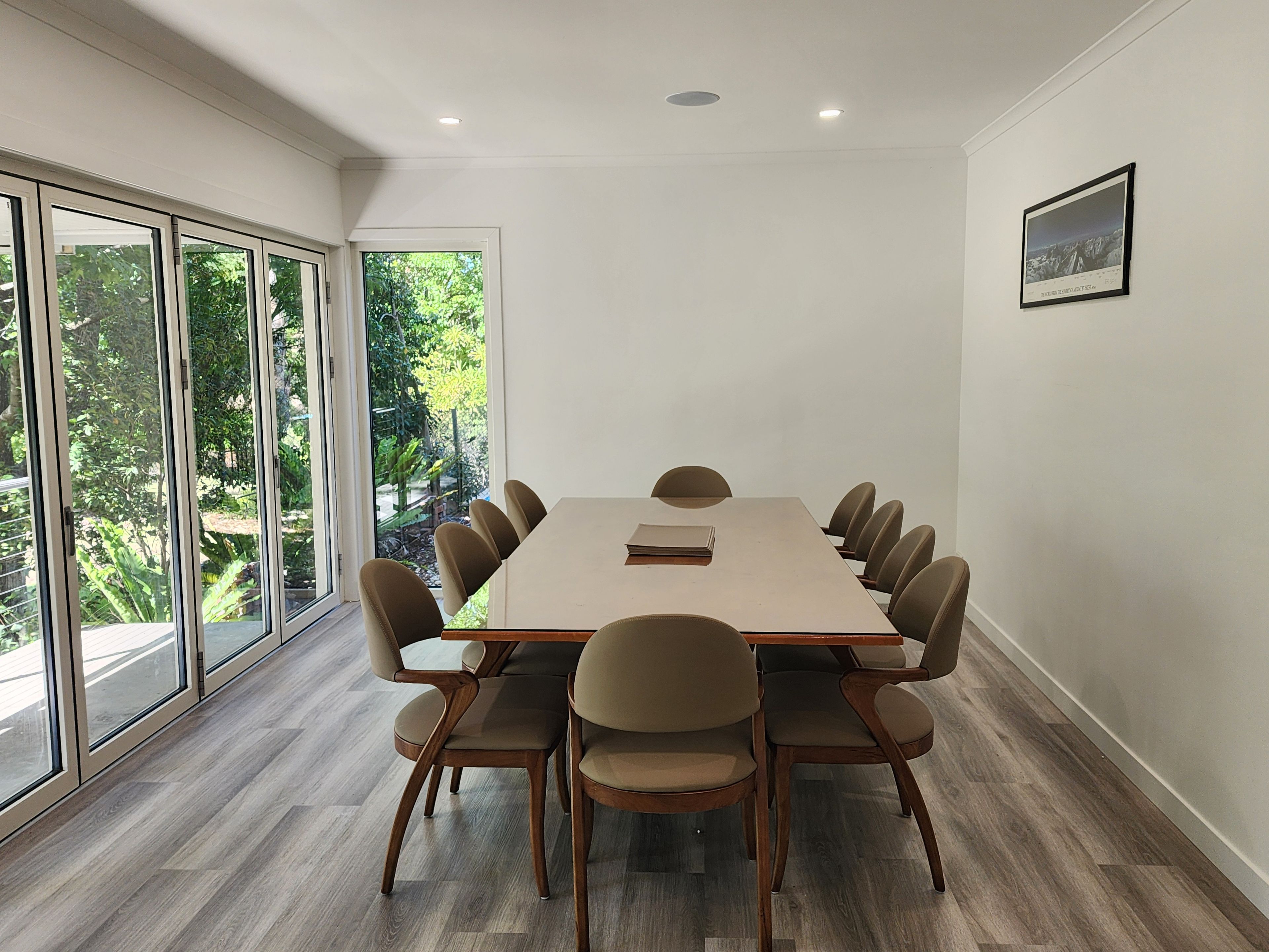 A conference room with a long table and chairs, large windows, and a framed picture on the wall.