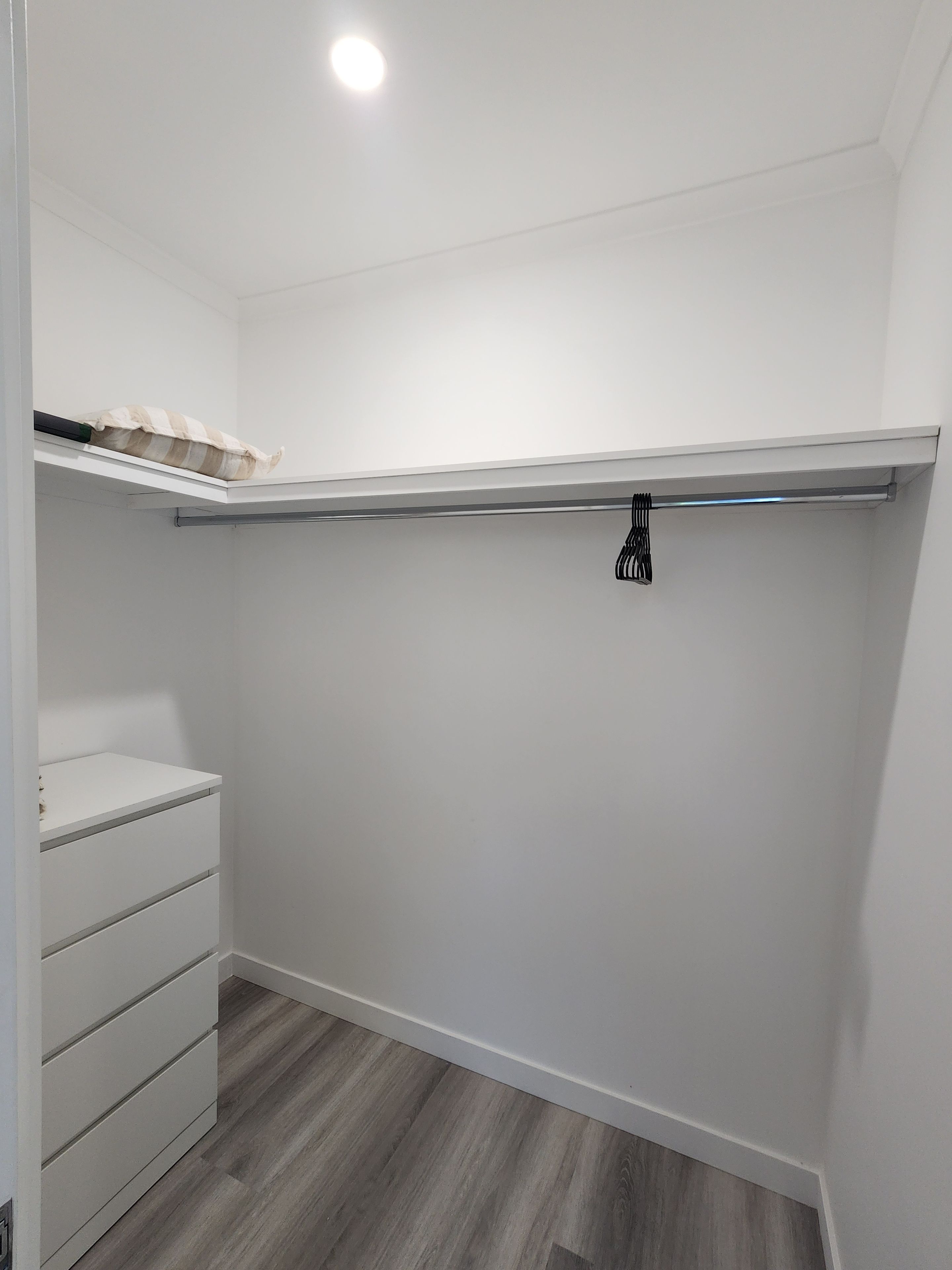 A closet with a white interior, a wooden floor, and a hanging rod.