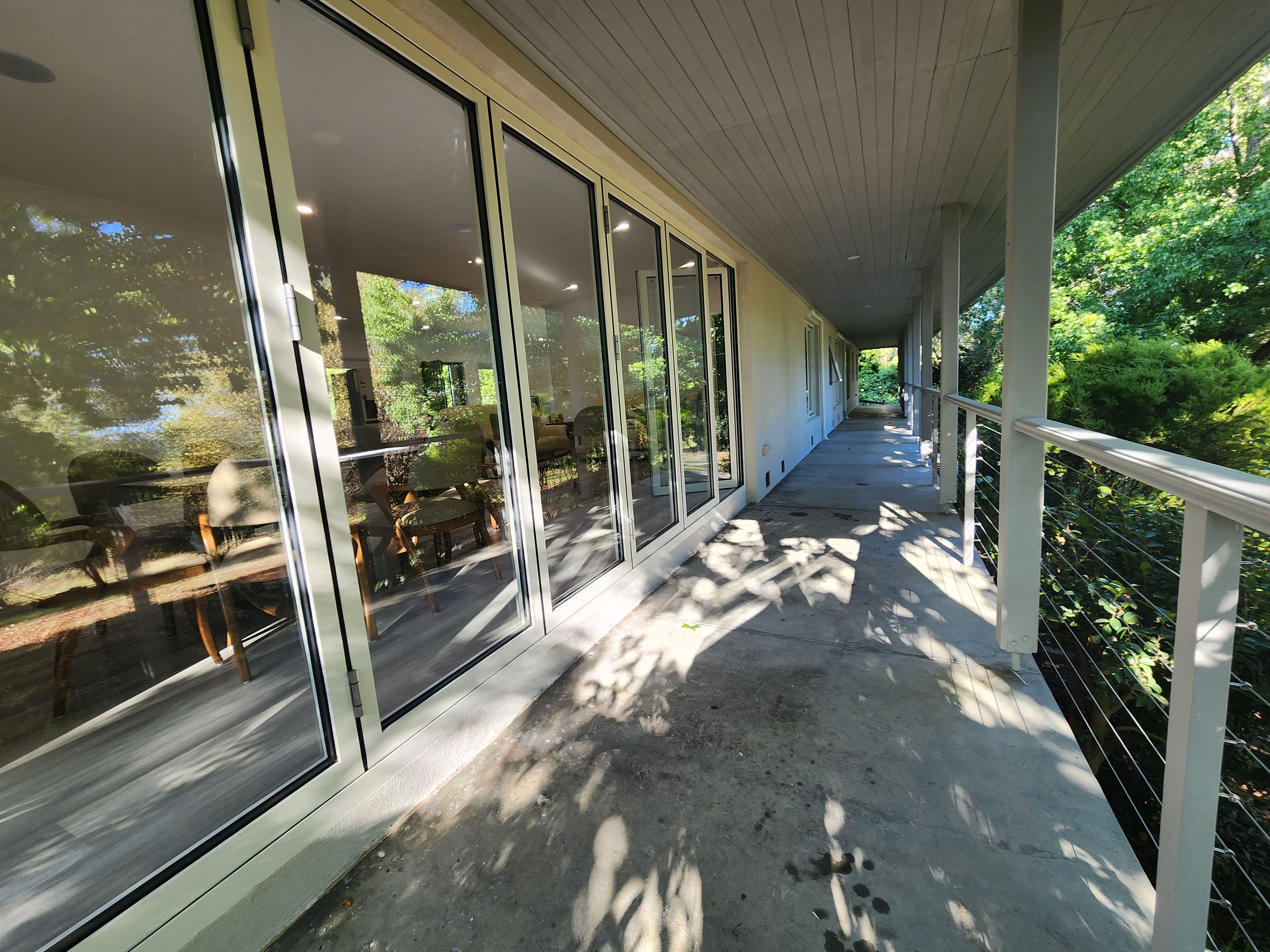A covered outdoor area with a concrete floor, large glass doors, and a metal railing.