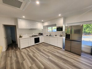 A modern kitchen with white cabinetry, a stainless steel refrigerator, and a wood floor.