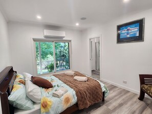 A bedroom with a bed, a piano, a shower, and a large window.