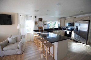 A modern kitchen with a central island, stainless steel appliances, and a seating area with a sofa and bar stools.