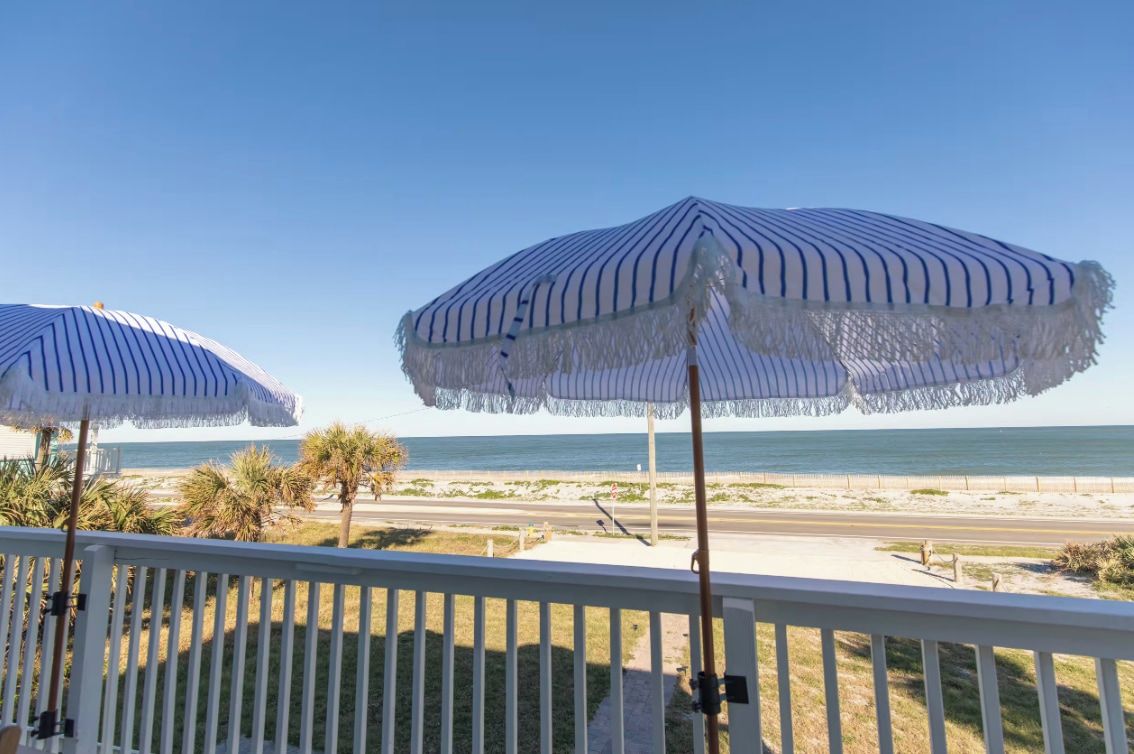 A balcony with two striped umbrellas overlooking a beach.