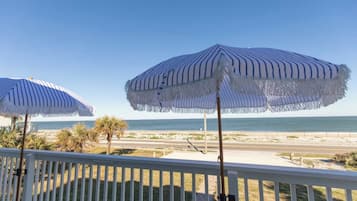 A balcony with two striped umbrellas overlooking a beach.