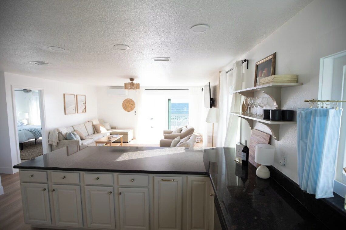 A modern kitchen with a central island, white cabinetry, and a view to a living area with a sofa and a dining table.